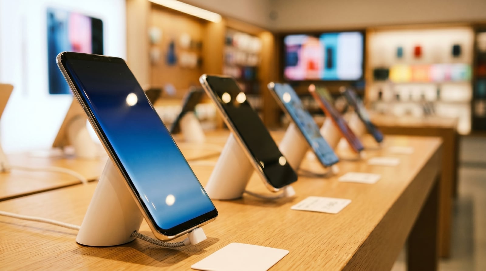Présentoir de téléphones sur une table en bois, au milieu d’un point de vente.