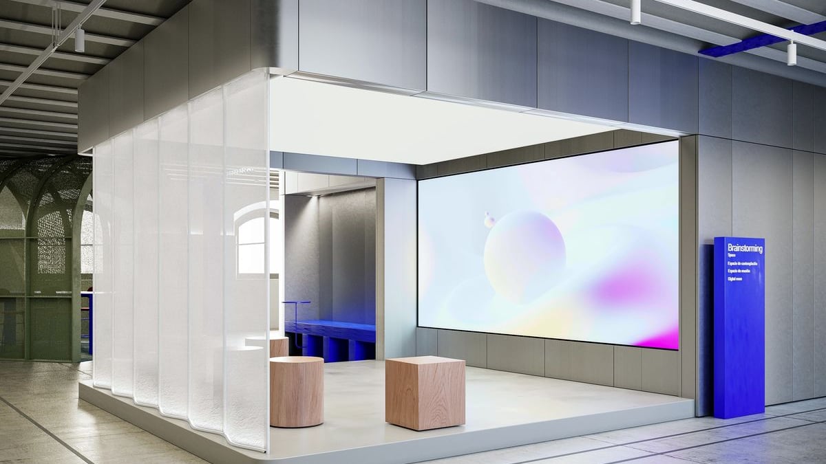 Stand aux cloisons translucides, écran d’animation et assises basses.